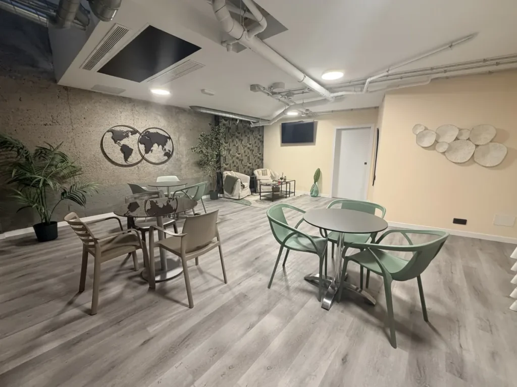 Zona de desayuno en la planta -1 de SAHERA: mesas con sillas verdes, plantas y un mapamundi en la pared