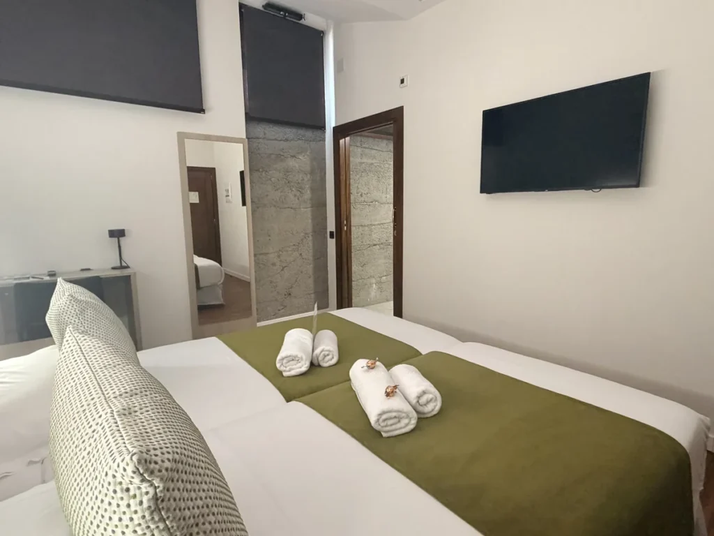 Camas de la habitación 101 con toallas y cojín, televisión en la pared y la puerta del baño