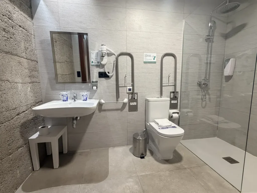 Baño adaptado de la habitación 101: lavabo accesible, barras de apoyo abatibles y ducha a ras de suelo