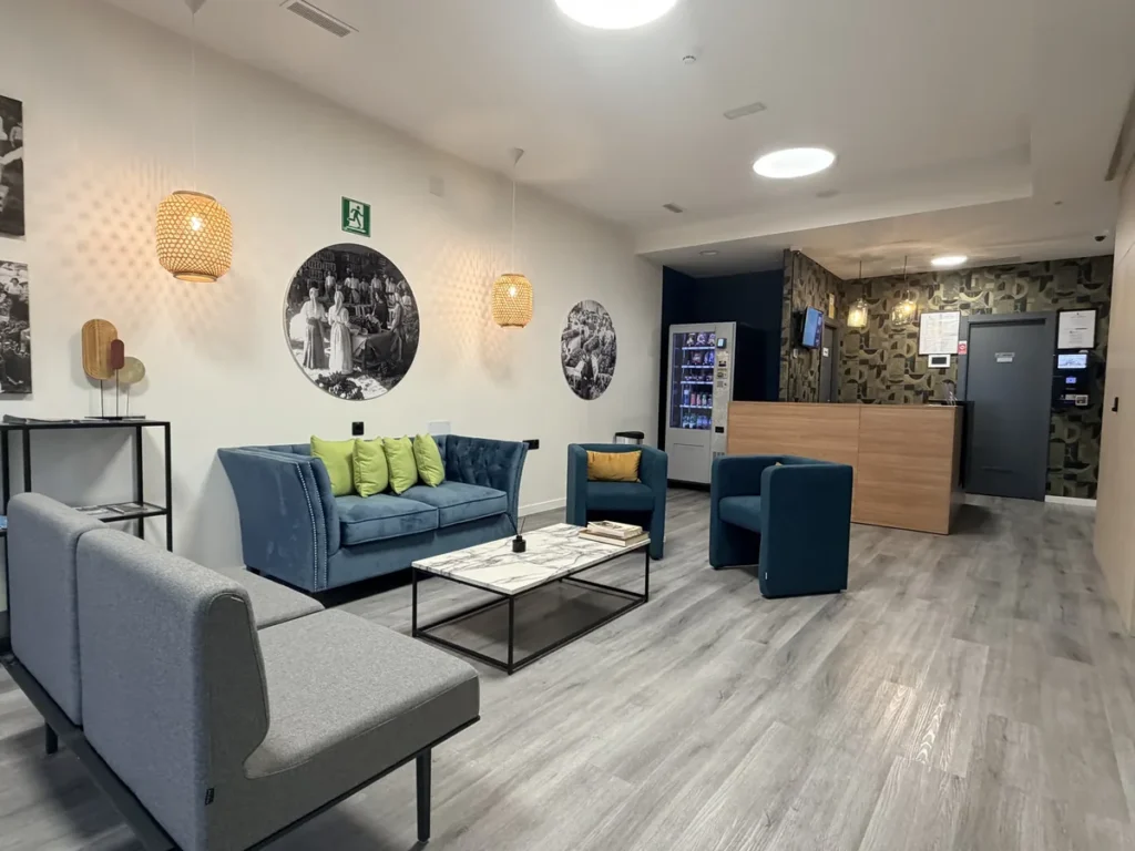 Zona de espera de la planta baja con sofás azules y grises, mesa baja y la recepción al fondo