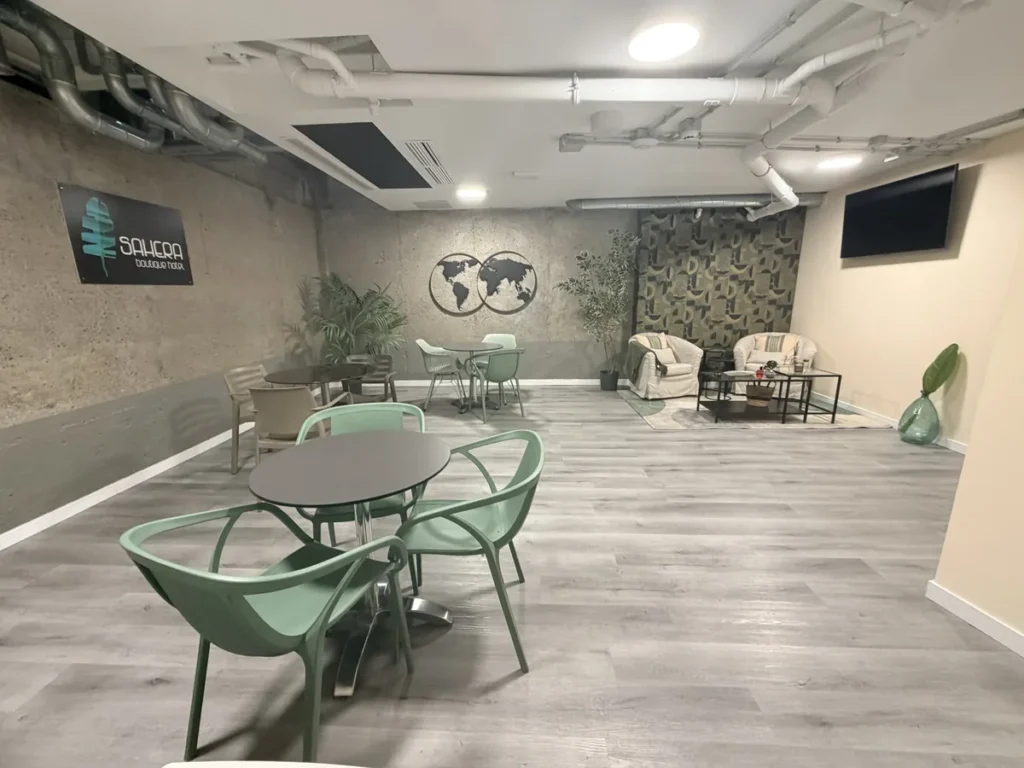 Salón de usos múltiples de SAHERA con mesas, sillas verdes, el logotipo del hotel y un rincón con sillones al fondo