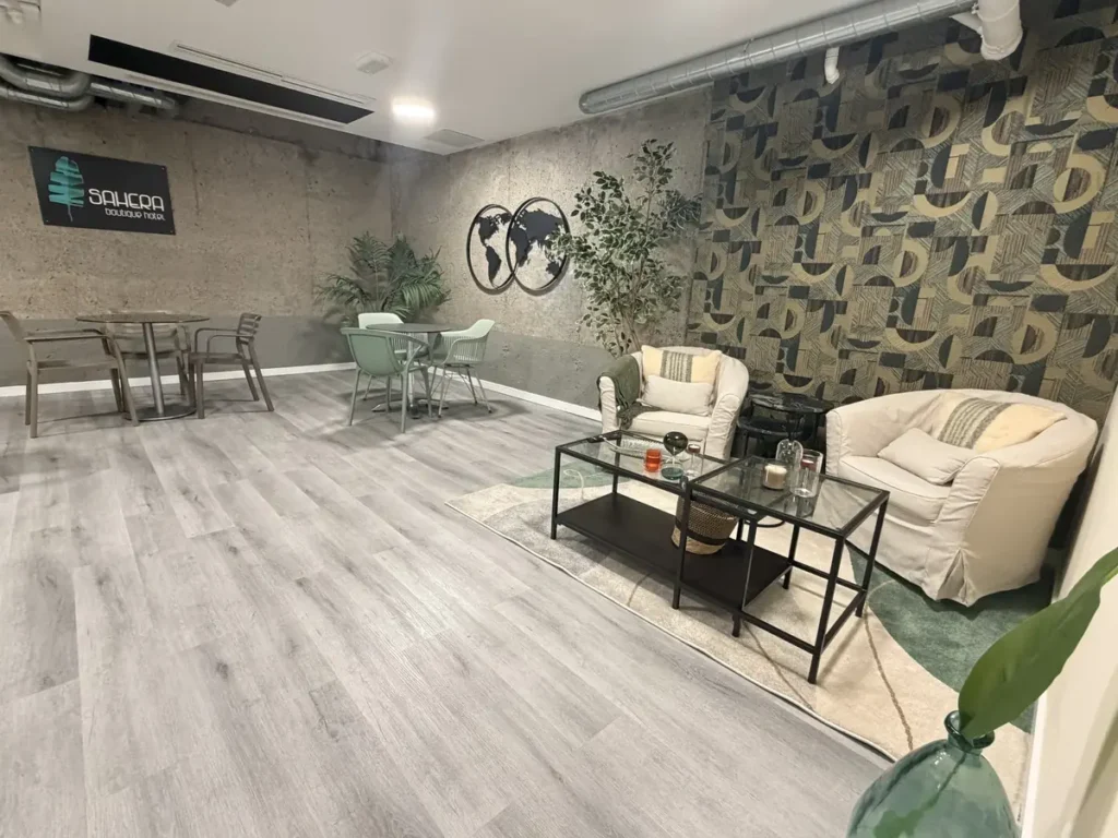 Sillones tapizados y mesa baja de cristal en el salón, con papel pintado geométrico verde